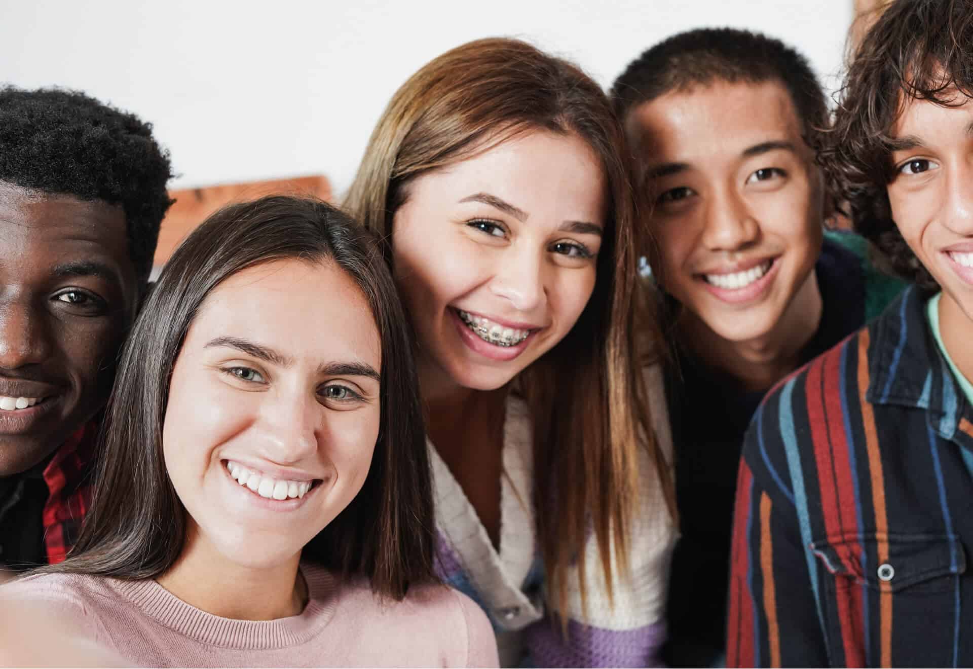 Positive multiracial teen friends taking selfie while walking in park